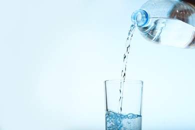 Pouring water from bottle into glass against blue background. Refreshing drink