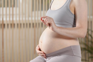 Photo of Pregnant woman taking pill indoors, closeup. Space for text