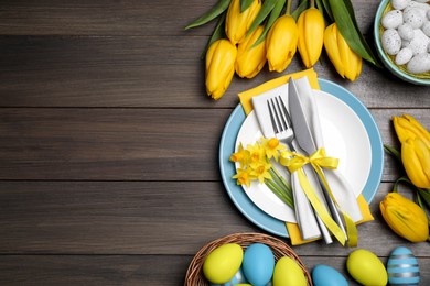 Photo of Festive table setting with flowers and painted eggs on wooden background, flat lay with space for text. Easter celebration