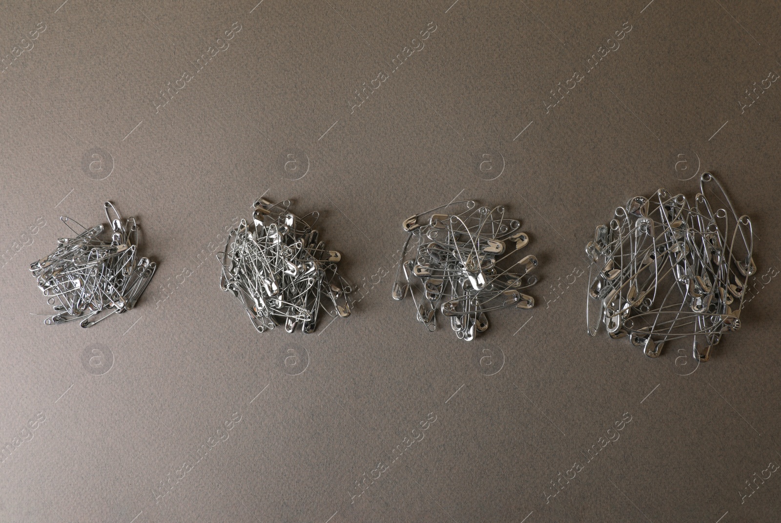 Photo of Piles of safety pins on grey textured background, flat lay