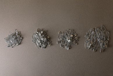 Photo of Piles of safety pins on grey textured background, flat lay