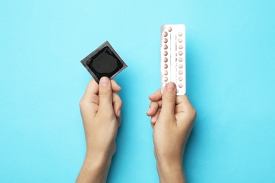 Woman holding condom and birth control pills on blue background, top view. Safe sex