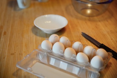 Photo of Carton with eggs, white plate and knife on wooden table