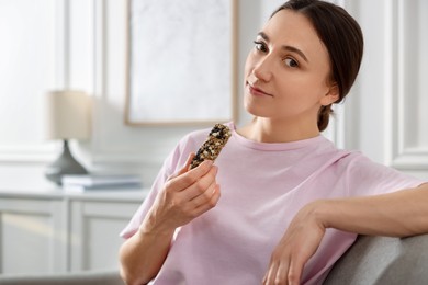 Woman holding tasty granola bar at home