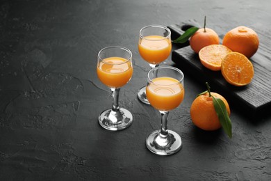 Photo of Tasty tangerine liqueur in glasses and fresh citrus fruits on black textured table. Space for text