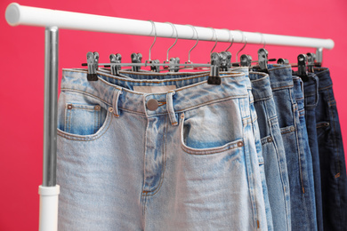 Photo of Rack with stylish jeans on pink background, closeup