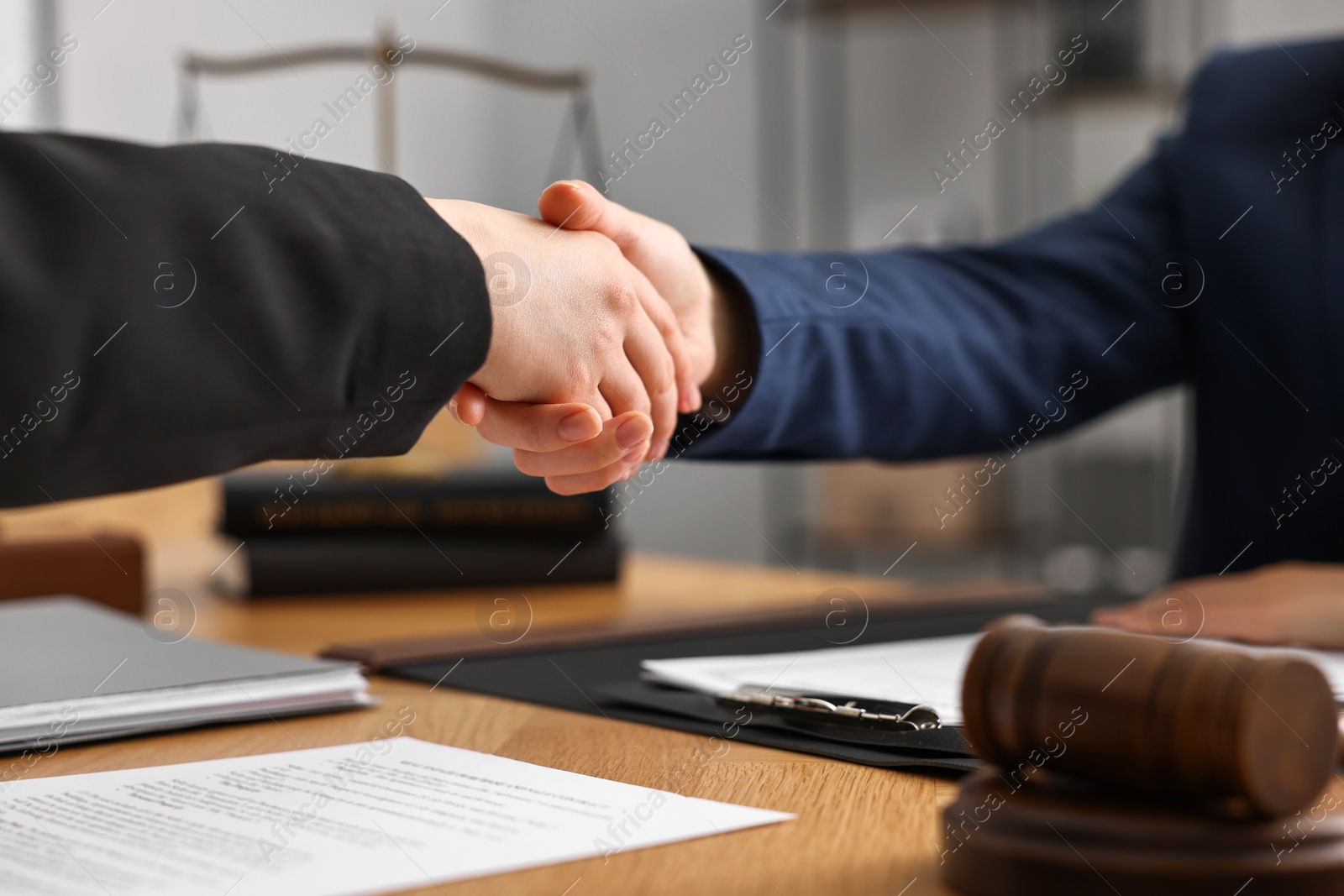 Photo of Notary shaking hands with client at wooden table in office, closeup