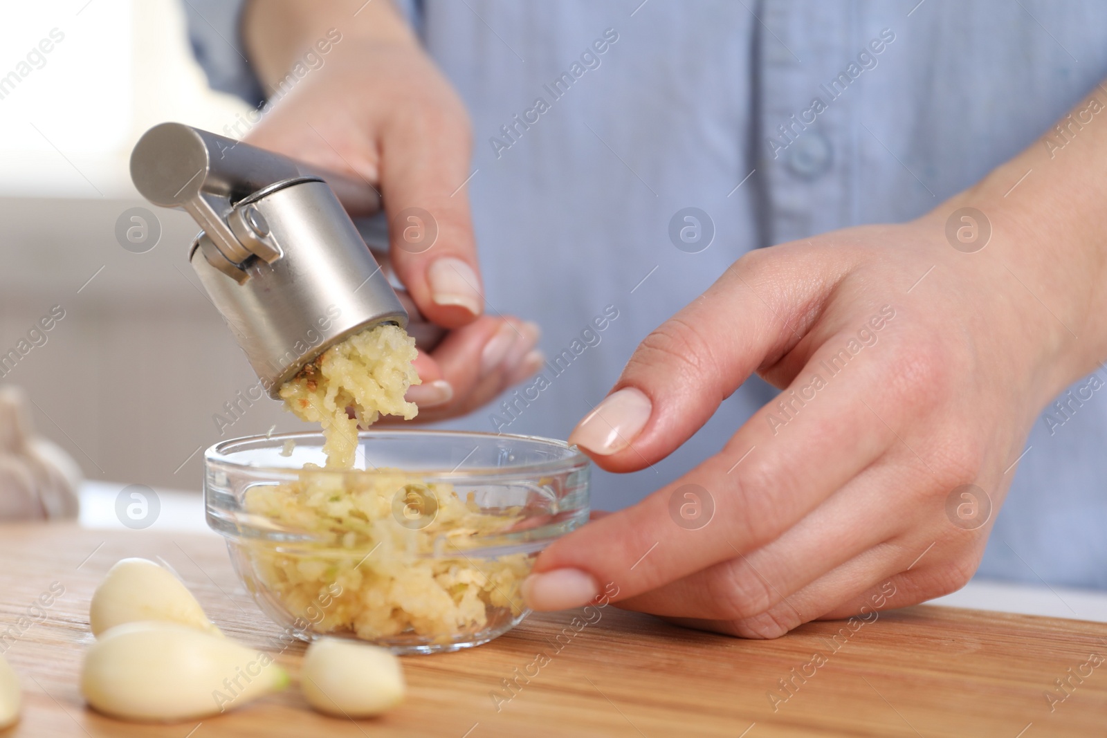 Photo of Woman squeezing garlic with press at wooden table indoors, closeup