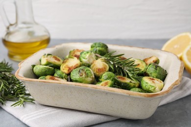 Photo of Delicious roasted Brussels sprouts and rosemary in baking dish on grey table, closeup