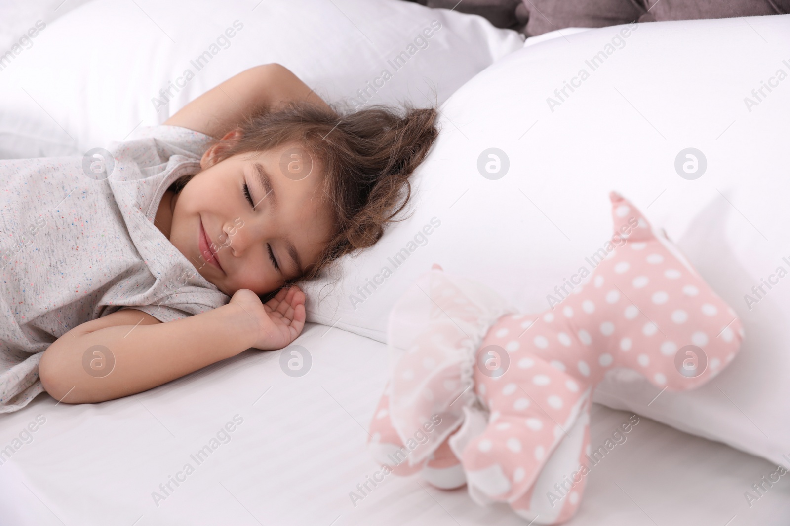 Photo of Cute little girl with toy sleeping on bed