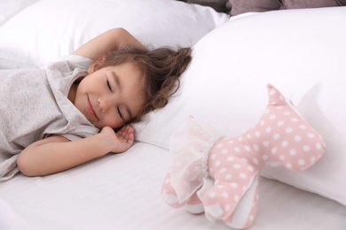 Cute little girl with toy sleeping on bed