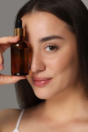 Beautiful young woman with essential oil on light grey background, closeup