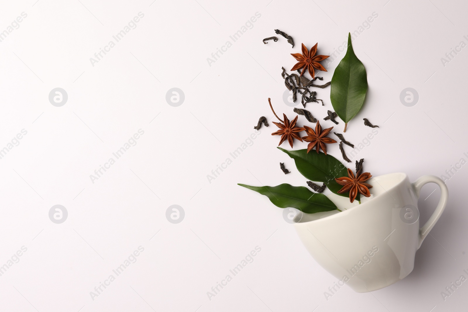 Photo of Anise stars, dry tea, green leaves and cup on white background, flat lay. Space for text