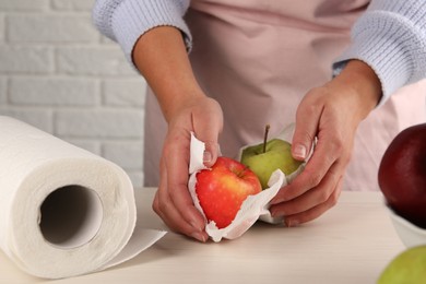 Photo of Woman wiping apples with paper towel at light wooden table, closeup