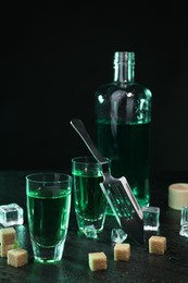 Photo of Absinthe in shot glasses, spoon, brown sugar and ice cubes on gray table against dark background. Alcoholic drink