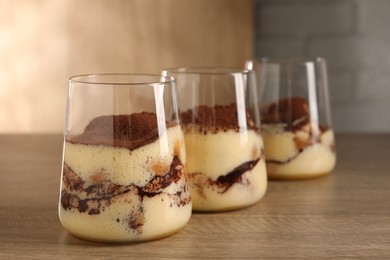 Photo of Delicious tiramisu in glasses on wooden table, closeup