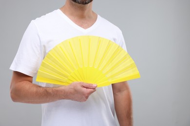 Photo of Man holding hand fan on light grey background, closeup. Space for text