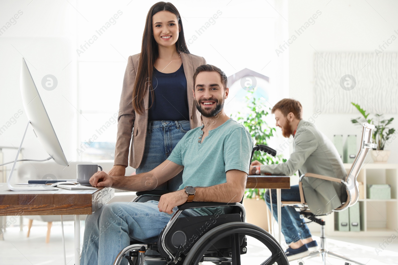 Photo of Young man in wheelchair with colleagues at workplace