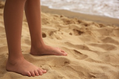 Photo of Little girl standing on sandy beach, closeup. Space for text