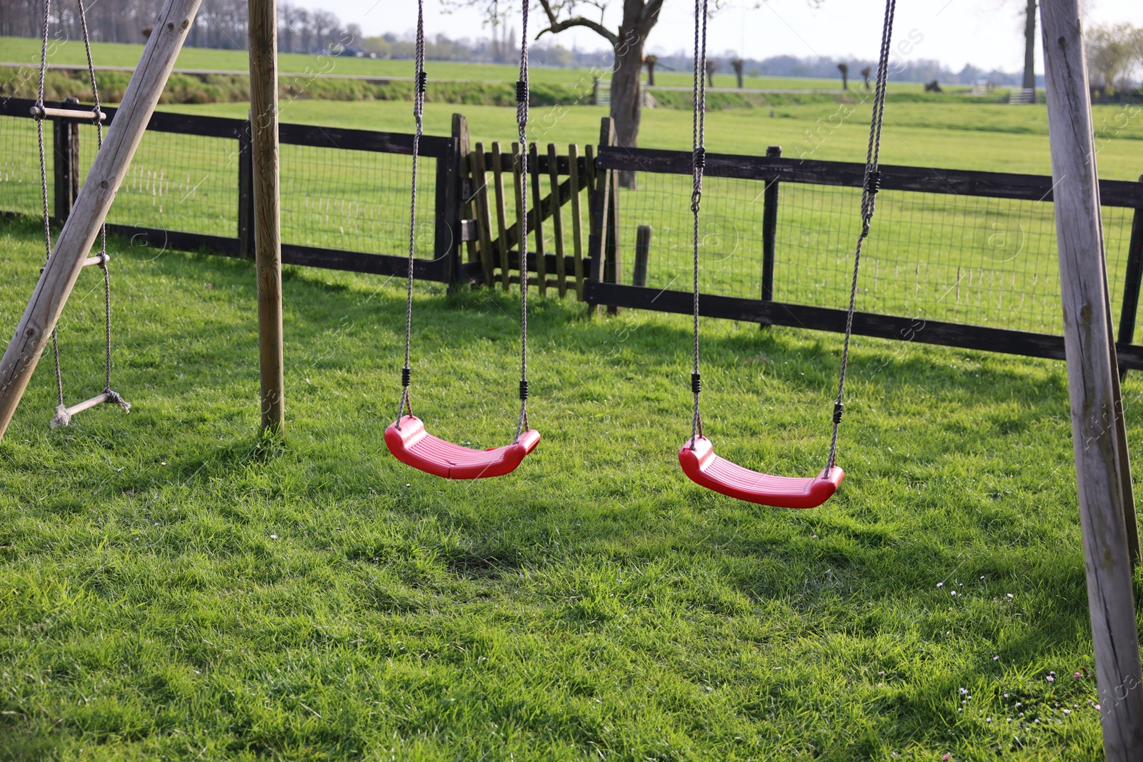 Photo of Outdoor swings on green grass near wooden fence outdoors