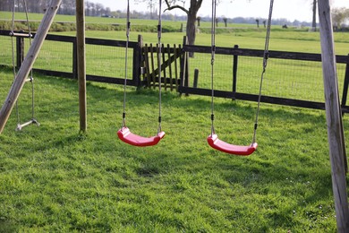 Outdoor swings on green grass near wooden fence outdoors