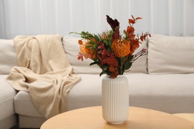 Vase with bouquet of beautiful leucospermum flowers on wooden coffee table near beige sofa in room, space for text