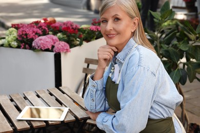 Happy business owner with tablet at table near her flower shop outdoors