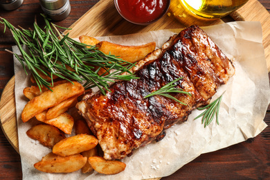 Photo of Delicious grilled ribs and garnish on wooden table, flat lay