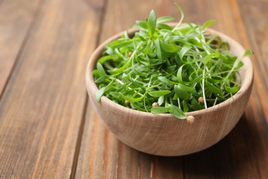 Photo of Bowl with fresh microgreen on wooden table, closeup