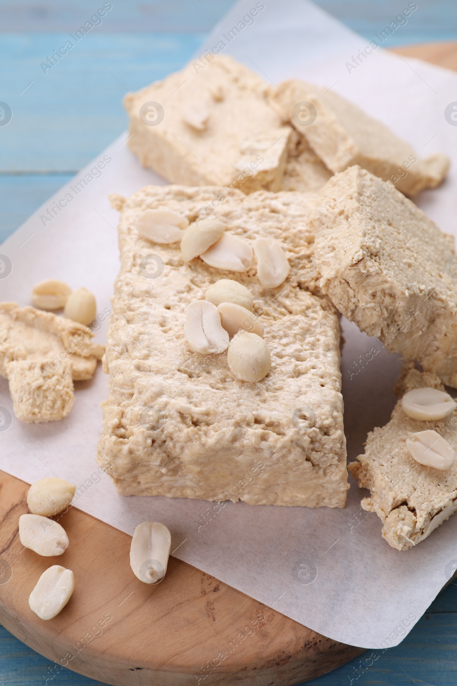 Photo of Pieces of tasty halva and peanuts on wooden board, closeup