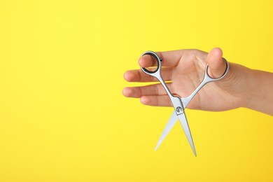 Photo of Hairdresser holding professional scissors and space for text on yellow background, closeup. Haircut tool