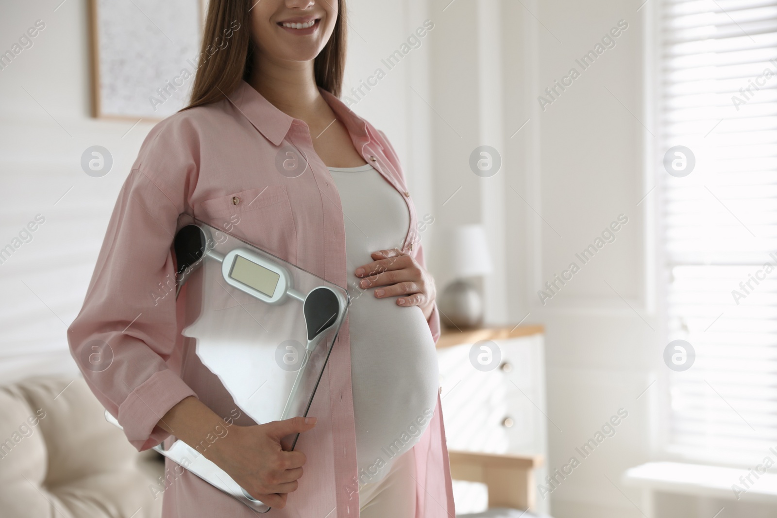 Photo of Young pregnant woman with scales at home, closeup