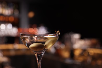 Photo of Martini glass with fresh cocktail and olives against blurred background. Space for text