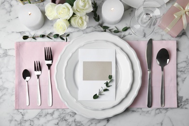 Elegant festive table setting with blank card on white marble background, flat lay