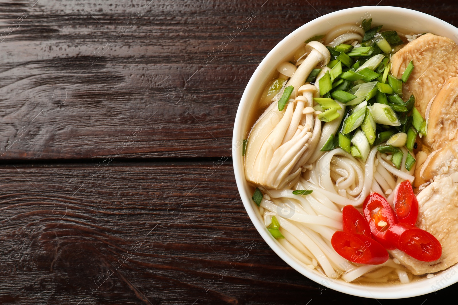 Photo of Delicious ramen with meat and mushrooms in bowl on wooden table, top view. Space for text