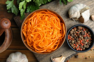 Photo of Delicious Korean carrot salad, garlic, spices and parsley on wooden table, flat lay