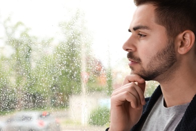 Photo of Thoughtful handsome man near window indoors on rainy day