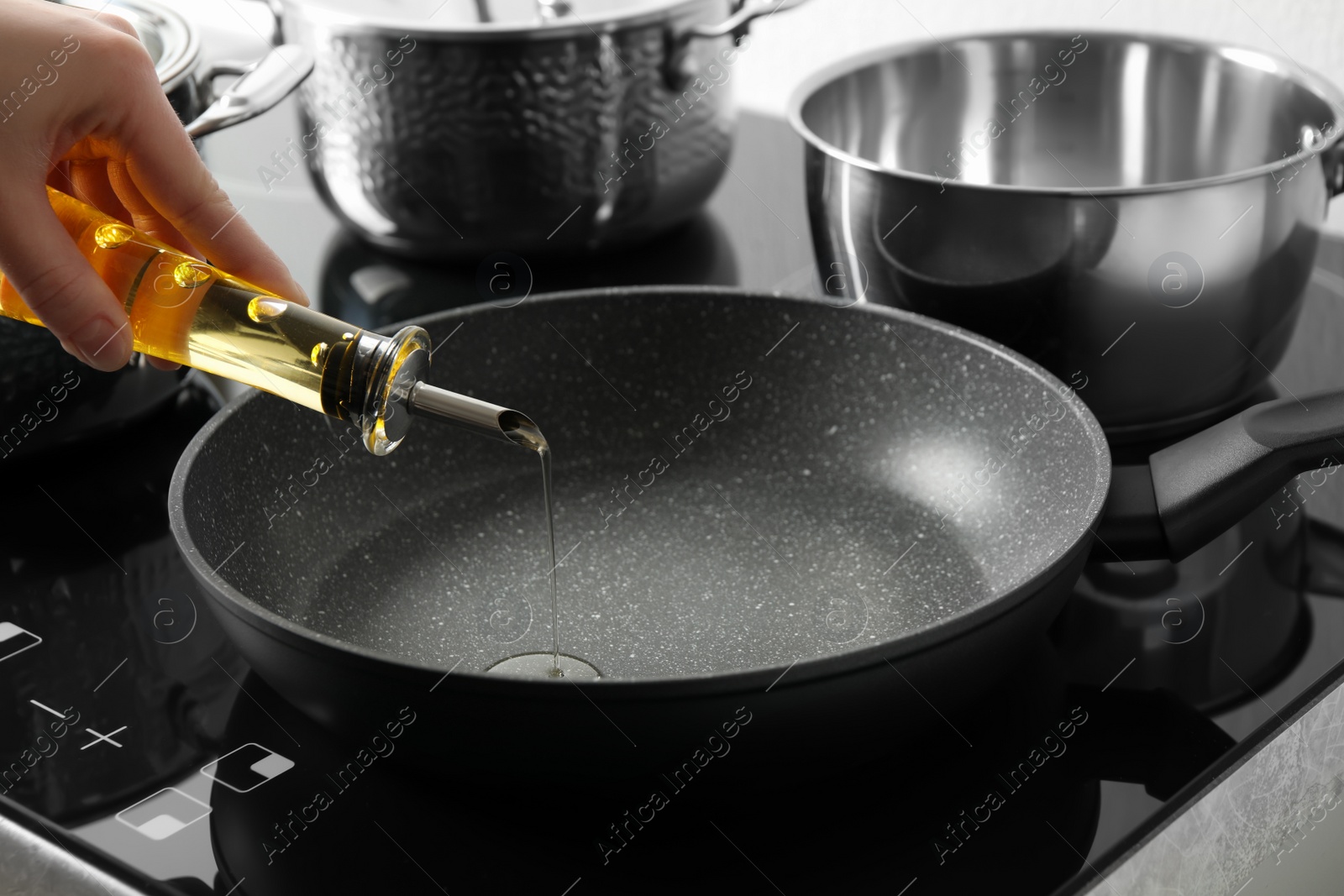 Photo of Woman pouring cooking oil from bottle into frying pan, closeup