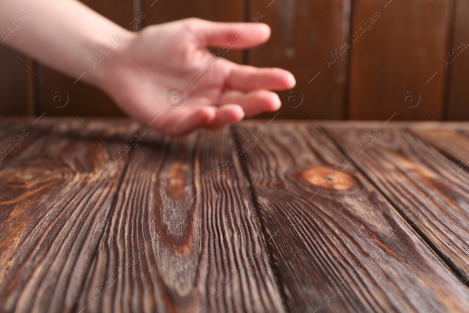 Photo of Woman holding hand above wooden table, selective focus. Space for text