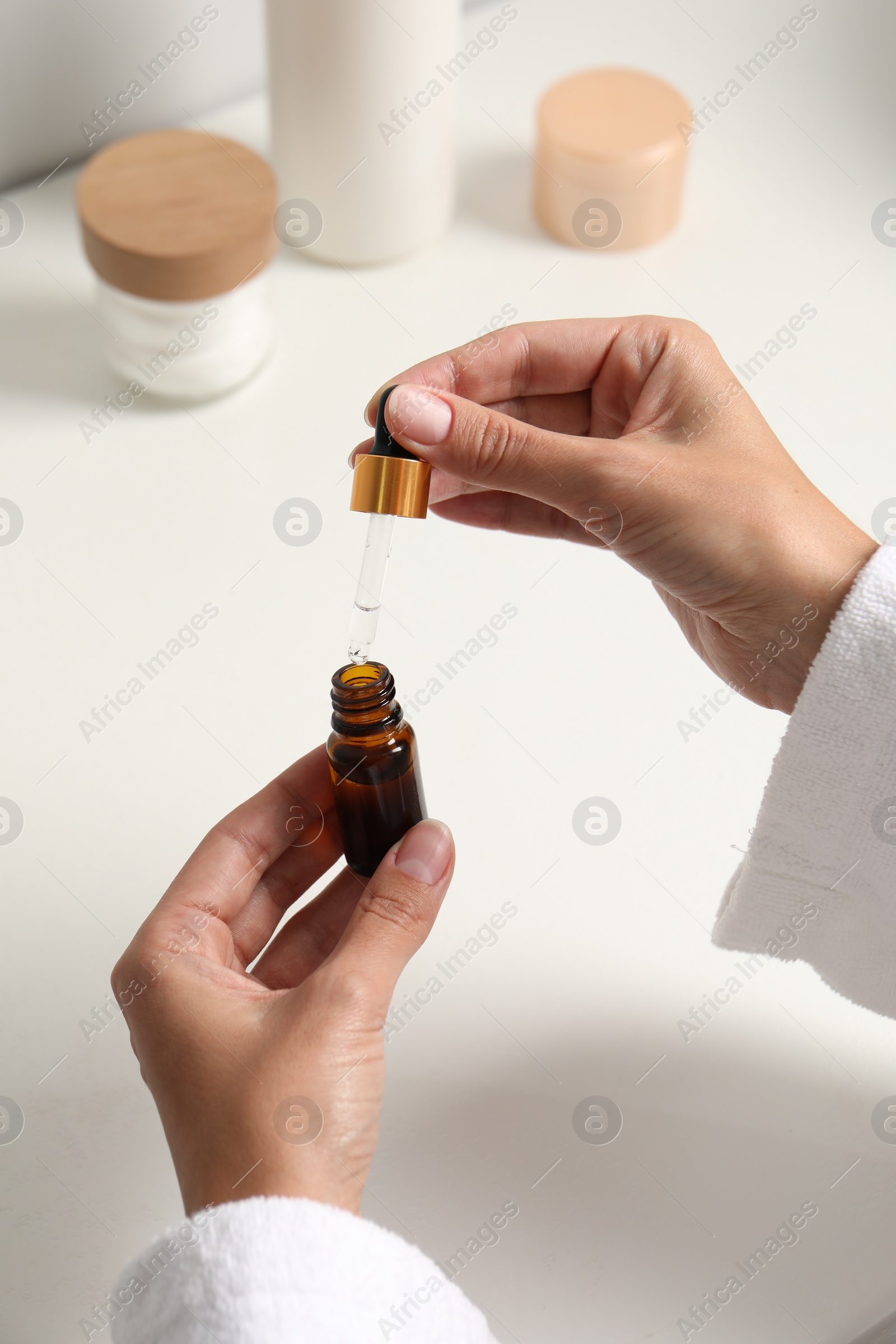 Photo of Woman with bottle of cosmetic serum and pipette at white table, closeup