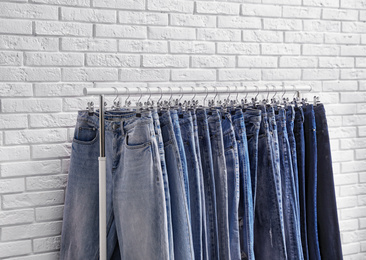 Rack with stylish jeans near brick wall, closeup