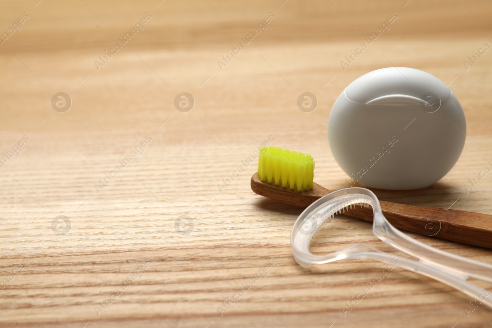 Photo of Tongue cleaner, dental floss and toothbrush on wooden table, closeup. Space for text