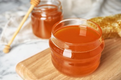 Photo of Glass jar with sweet honey on wooden board, closeup