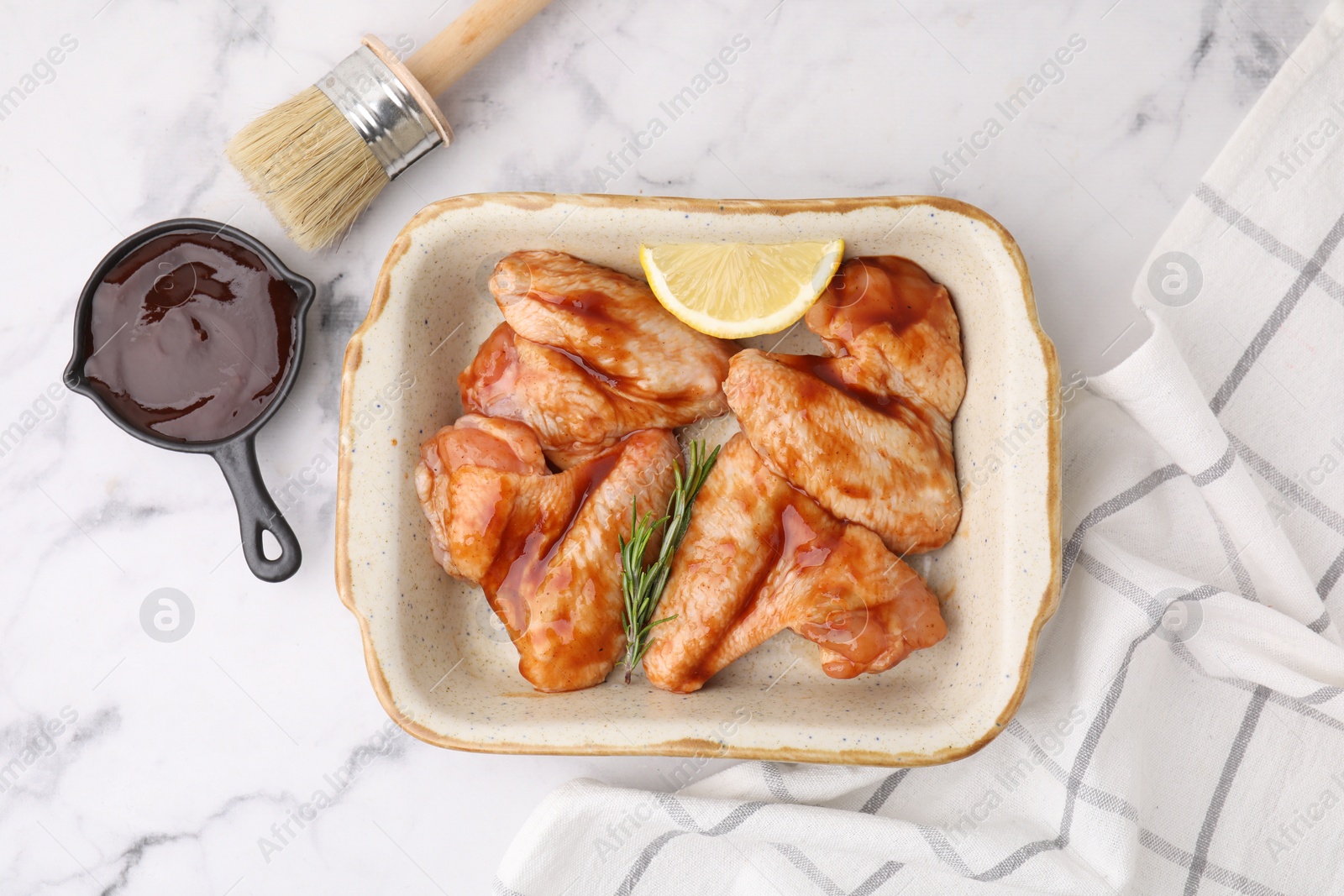 Photo of Fresh marinade, basting brush, raw chicken wings, rosemary and lemon on white marble table, flat lay