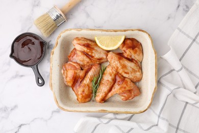 Photo of Fresh marinade, basting brush, raw chicken wings, rosemary and lemon on white marble table, flat lay