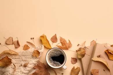 Flat lay composition with cup of hot drink, books and autumn leaves on beige background, space for text. Cozy atmosphere