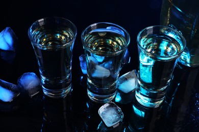 Alcohol drink in shot glasses and ice cubes on mirror surface