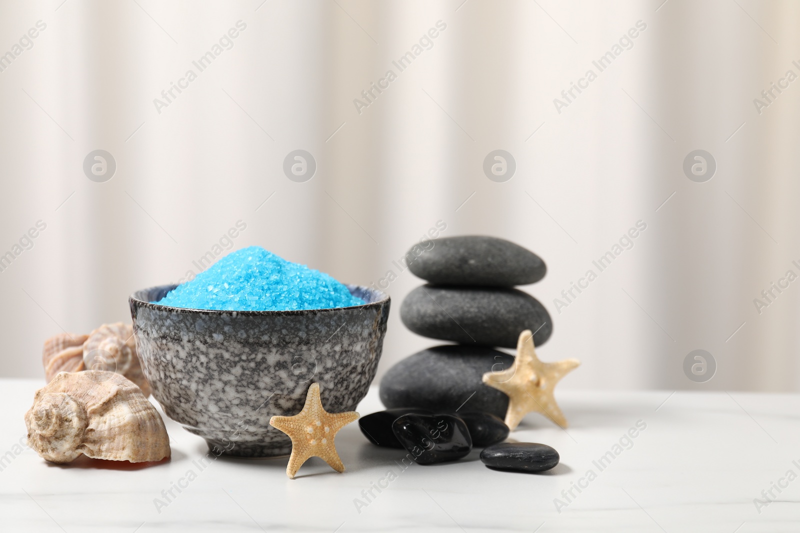 Photo of Light blue sea salt in bowl, spa stones, starfishes and shells on white table, space for text