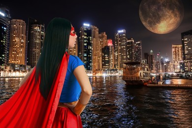 Image of Confident young woman wearing superhero costume and beautiful cityscape in night on background