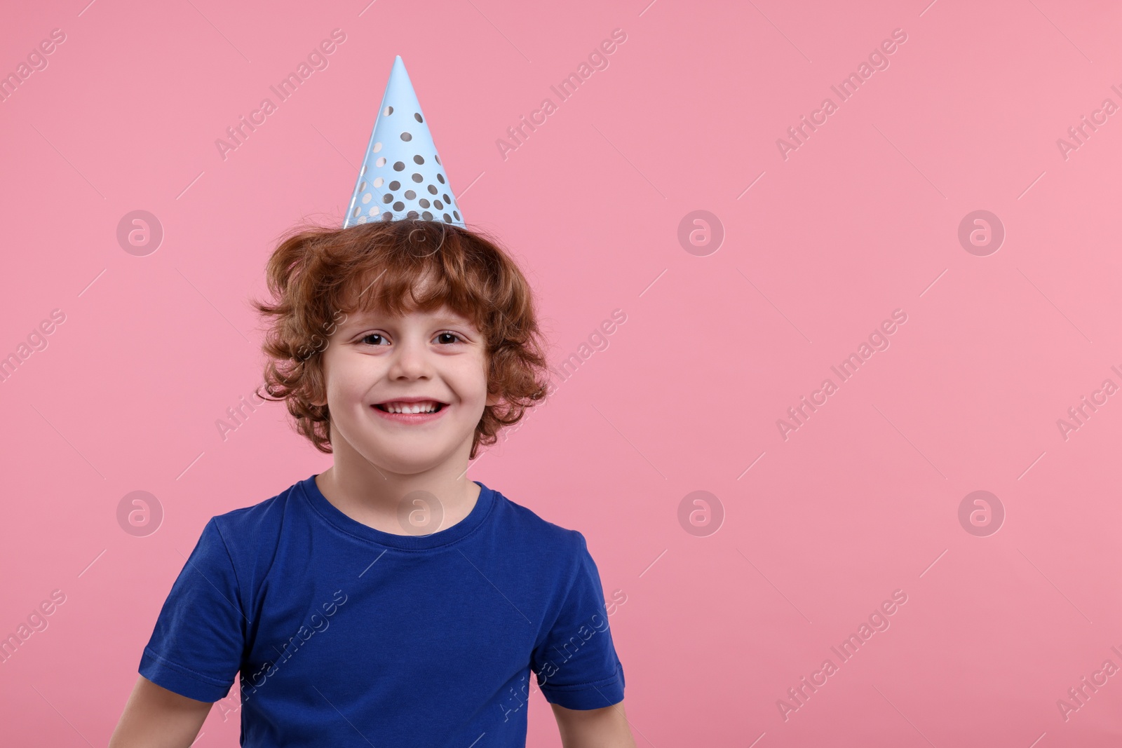 Photo of Happy little boy in party hat on pink background. Space for text